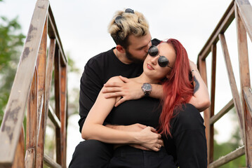 Stylish couple in love in black clothes are walking in the park and hugging. Lovely hipster couple smiling and enjoying time together. Youth, love and lifestyle concept