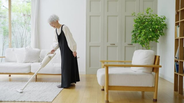 部屋でハンディ掃除機をかけるシニア女性（掃除・家事）