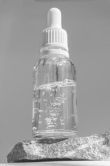 Serum in clear glass bottle with dropper lid on stand made of natural granite stone. Essential oil...