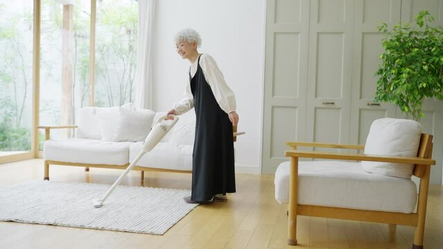 部屋でハンディ掃除機をかけるシニア女性（掃除・家事）