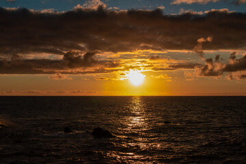 Naklejka na ściany i meble Watching the sunset at the port of Puerto de la Cruz, Tenerife, Canary Islands, Spain, Europe. View of the horizon of Atlantic Ocean. The sun is reflecting in the calm sea. Vibrant clouds in the sky