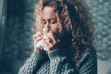 Fototapeta na wymiar Side view of woman blowing nose for flu influenza symptoms in winter at home. Temperature reduction indoor to save energy gas costs. Female people with virus contagion using paper tissues. Disease