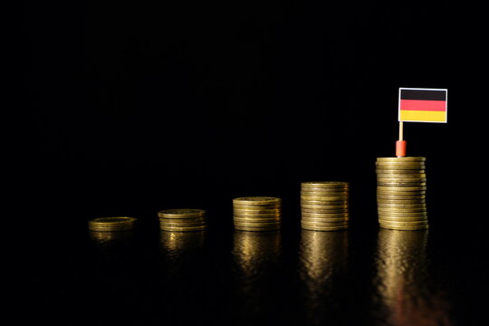 Germany economic growth, recovery after financial crisis and currency appreciation concept. German flag in increasing stack of coins in dark black background.