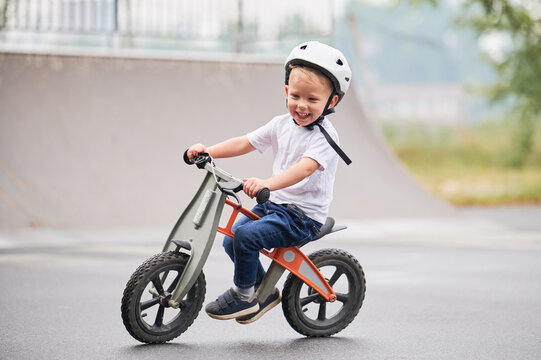 Smiling child riding balance bike. Male toddler kid in helmet learning to ride on run bicycle at skate park.