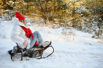 Beautiful young woman wearing a warm winter clothes, sitting on a sleigh and sliding down the hill, having fun on a snowy winter day