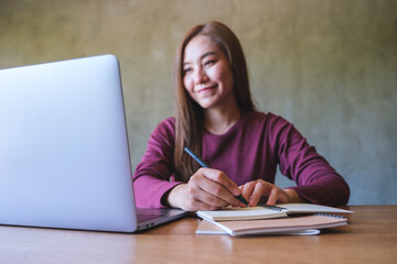 Portrait image of a business woman writing on a notebook while working on laptop computer