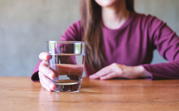 Closeup image of a young woman holding a glass of water on wooden table