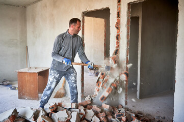Repairman crashing brick wall with sledgehammer, pieces of brick flying away from strong blow....