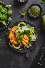 Summer salad with melon, cucumber, avocado, basil and red onion.
