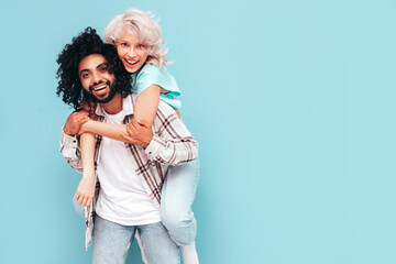 Smiling beautiful woman and her handsome boyfriend. Sexy cheerful multiracial family having tender moments on beige background in studio. Multiethnic models gives piggyback riding. Sitting on back