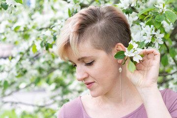 young woman with pink hair poses by a blooming apple tree.