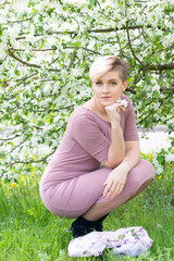 young woman with pink hair poses by a blooming apple tree.