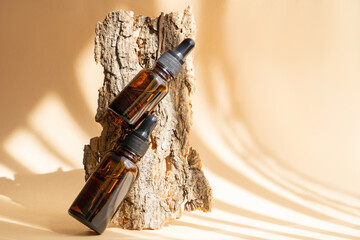 Mockup of amber-colored glass bottles with dropper lid on background of tree bark. Unmarked...
