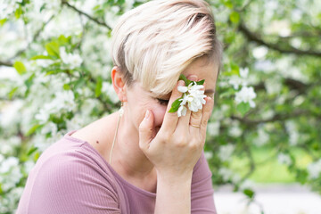 young woman with pink hair poses by a blooming apple tree.