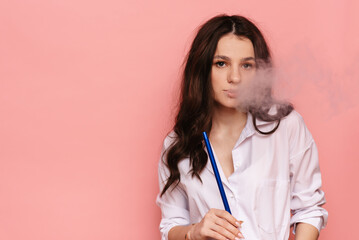 Young woman smokes a hookah, sheesha on a pink background. The pleasure of smoking.
