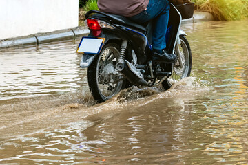 Man ride motorcycle passing through flooded road. Riding motorbike on flooded road during flood caused by torrential rains. Flooded road with large puddle. Splash by motorcycle through flood water.