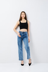 Young woman in black tank top and wide jeans leaning to the wall