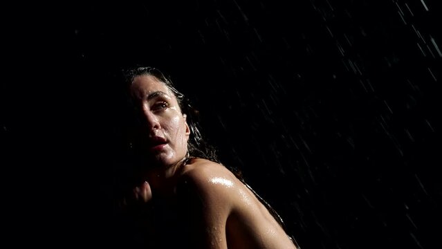 naked woman in the rain. side light. dark key. black background