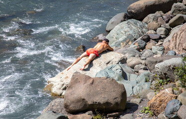 A man lies on the rocks near a mountain river