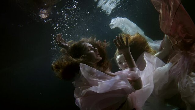 two women are floating in translucent fabrics in the dark under water. close-up