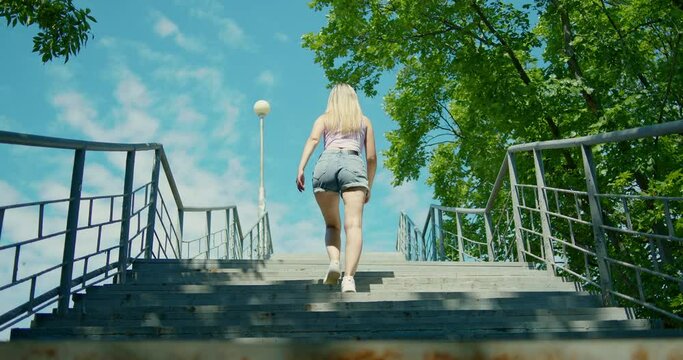 A young girl climbs a long concrete staircase up, in shorts, sneakers, sunglasses.