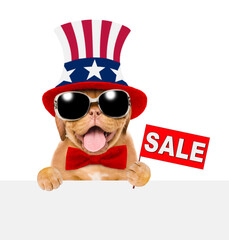 Happy Mastiff puppy wearing like Uncle Sam looks above empty white banner and shows signboard with labeled "sale". isolated on white background