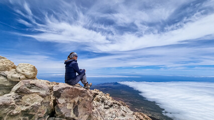 Rear view on hiking woman sitting on rock enjoying panorama from summit of volcano Pico del Teide...