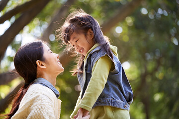 young asian mother talking to daughter outdoors in park