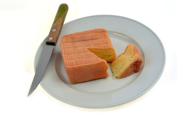 Fromage Maroilles entamé dans une assiette avec un couteau en gros plan sur fond blanc