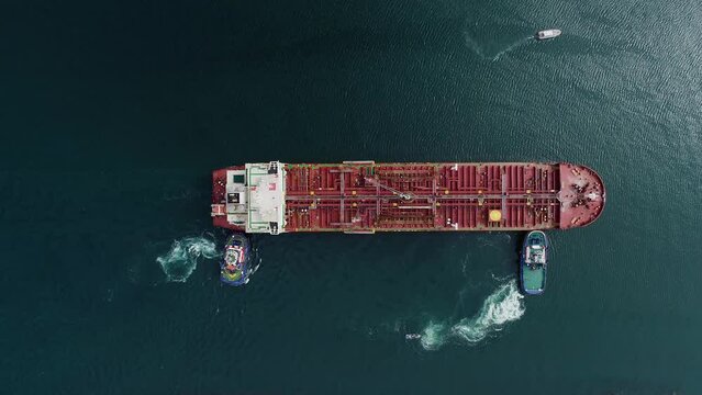Aerial view above boats pushing an empty cargo ship, towards the harbor - top down, drone shot