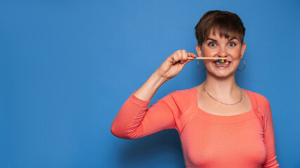 A smiling young woman holds a natural bamboo toothbrush, isolated on a blue background. The concept of oral hygiene. A place for your text.