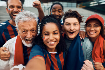 Group of happy sports fans taking selfie while going on soccer match together.