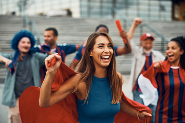 Cheerful woman has fun while celebrating with group of soccer fans outdoors.