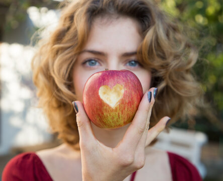 healthy eating - young woman holds a red apple in front of her face with a heart cut out in it. selective focus. proper vitamin nutrition. love concept. health 