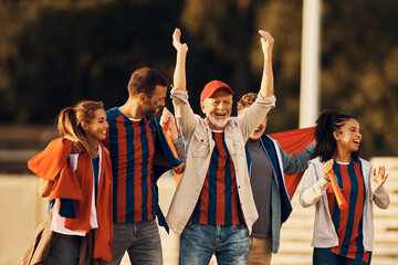 Group of cheerful fans having fun on street while going on soccer match.