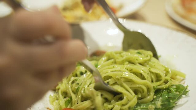 A woman stirs pasta with a fork and spoon in a plate. Close-up.