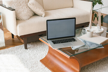 Modern Scandinavian interior. Stylish coffee table, laptop, book in fabric cover, white sofa. Minimalistic home interior.