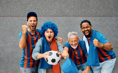 Group of passionate fans cheering for their team during soccer championship and looking at camera.