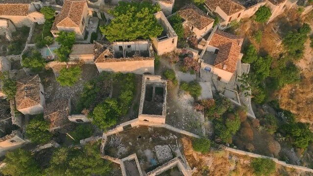 Aerial view of partly abandoned mountain village of Qeparo, situated on a rocky outcrop above Borsh Bay, Albania. Scenic view from a drone circling an ancient village illuminated by the orange light.