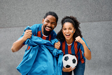 Cheerful black couple cheering for their soccer team and looking at camera.