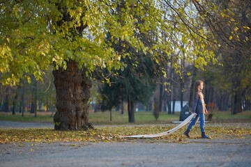 Fototapeta premium A girl in a knitted sweater in the autumn park is walking along the path. September or October, yellow leaves on trees.
