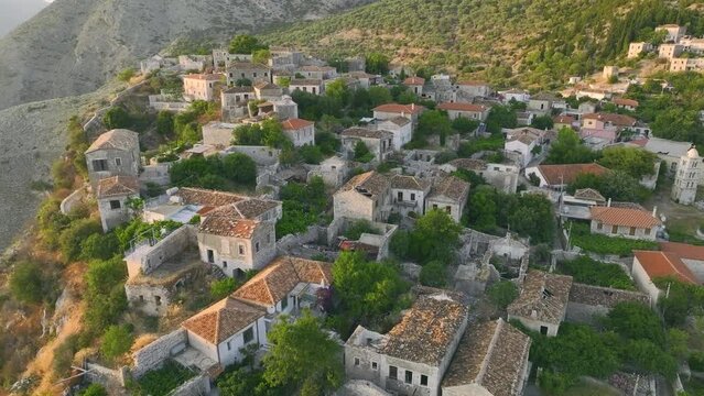 Aerial view of partly abandoned mountain village of Qeparo, situated on a rocky outcrop above Borsh Bay, Albania. Scenic view from a drone circling an ancient village illuminated by the orange light.