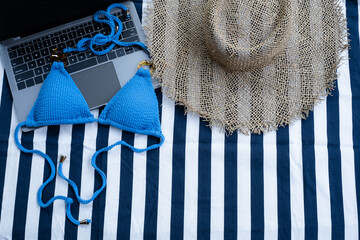 Top view of blue bikini, laptop and panama hat on the beach blanket for picnic on the beach. Summer vacation, summer in holiday concept. Online freelance concept.