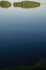 Vertical photo of calm lake water and green islands on the horizon