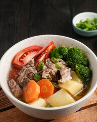 Soup, Sop Daging with vegetables is Indonesian traditional food, served in bowl, on the wooden table. Close up and selective image focus.
