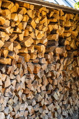 Oak chopped firewood is neatly stacked. Alternative and cheap fuel for stove instead of gas. Stack of firewood is protected from rain. Close-up of chopped firewood stacked to dry in sun.