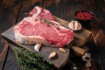 Prime T-bone beef meat steak, raw porterhouse steak on butcher board with herbs. Wooden background....