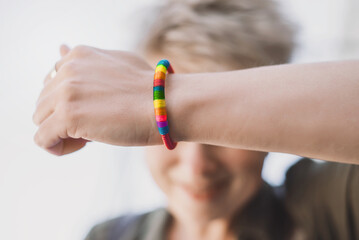 A young blonde woman with a short haircut shows a close-up of a rainbow bracelet LGBT symbol....
