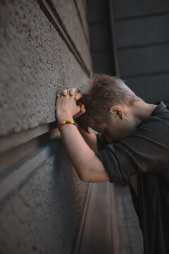 A young blonde woman with a short haircut shows a close-up of a rainbow bracelet LGBT symbol. The girl is crying on the street, covering her face with her hands. Desperate situation and stress
