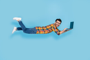Full body profile portrait of excited cheerful man fly levitate use netbook isolated on blue color...